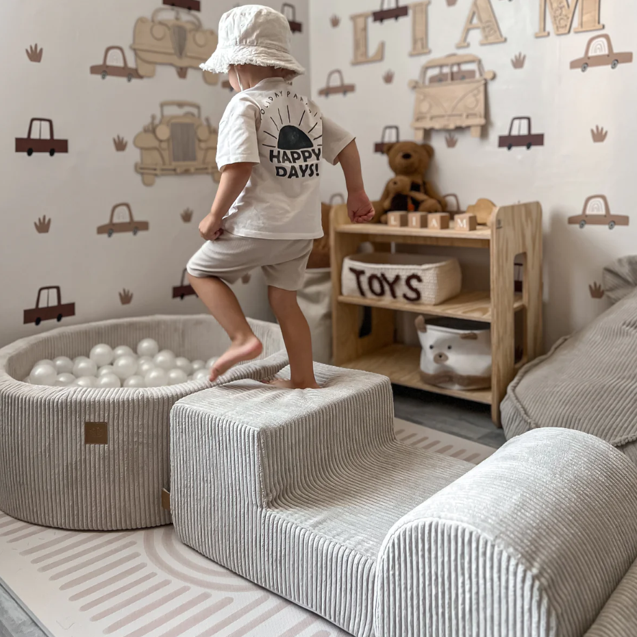 Child playing in a room with toys and furniture, featuring a 'Happy Days' t-shirt.