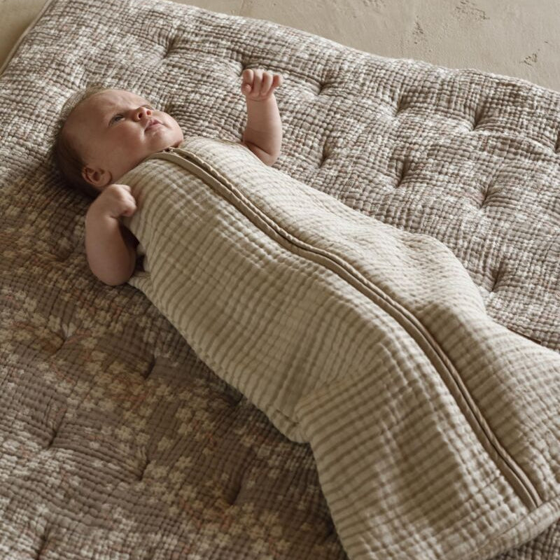 Baby wrapped in a beige swaddle on a textured surface