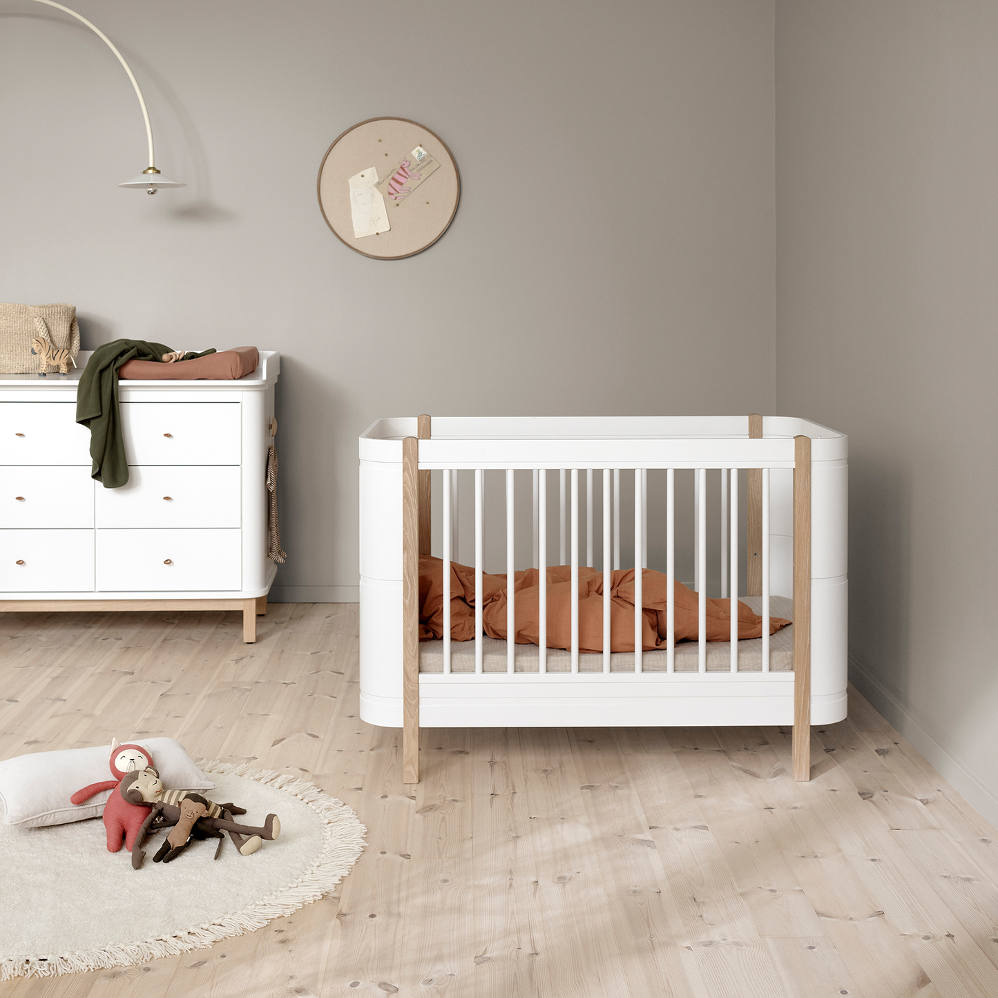 Nursery room with a white crib and dresser against a gray wall.