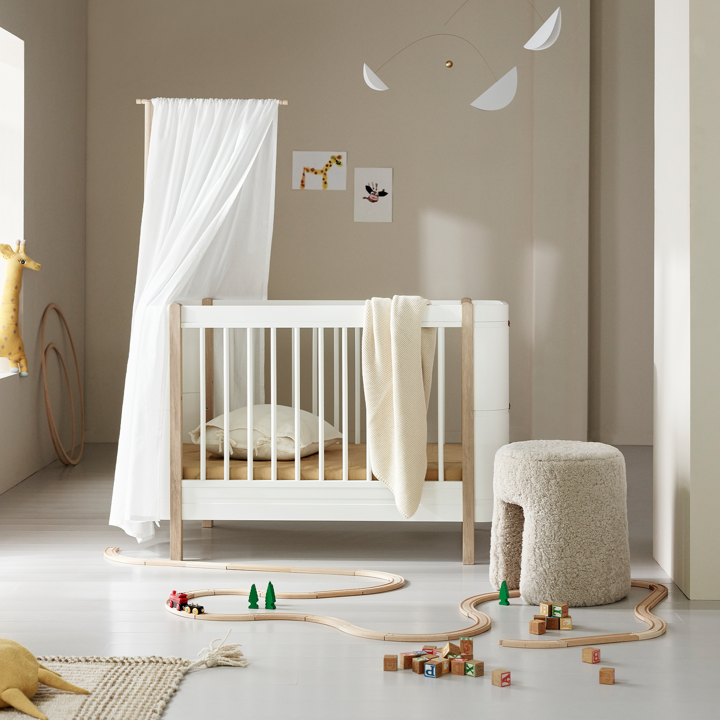 Modern nursery with a white crib, toys on the floor, and decorative elements.
