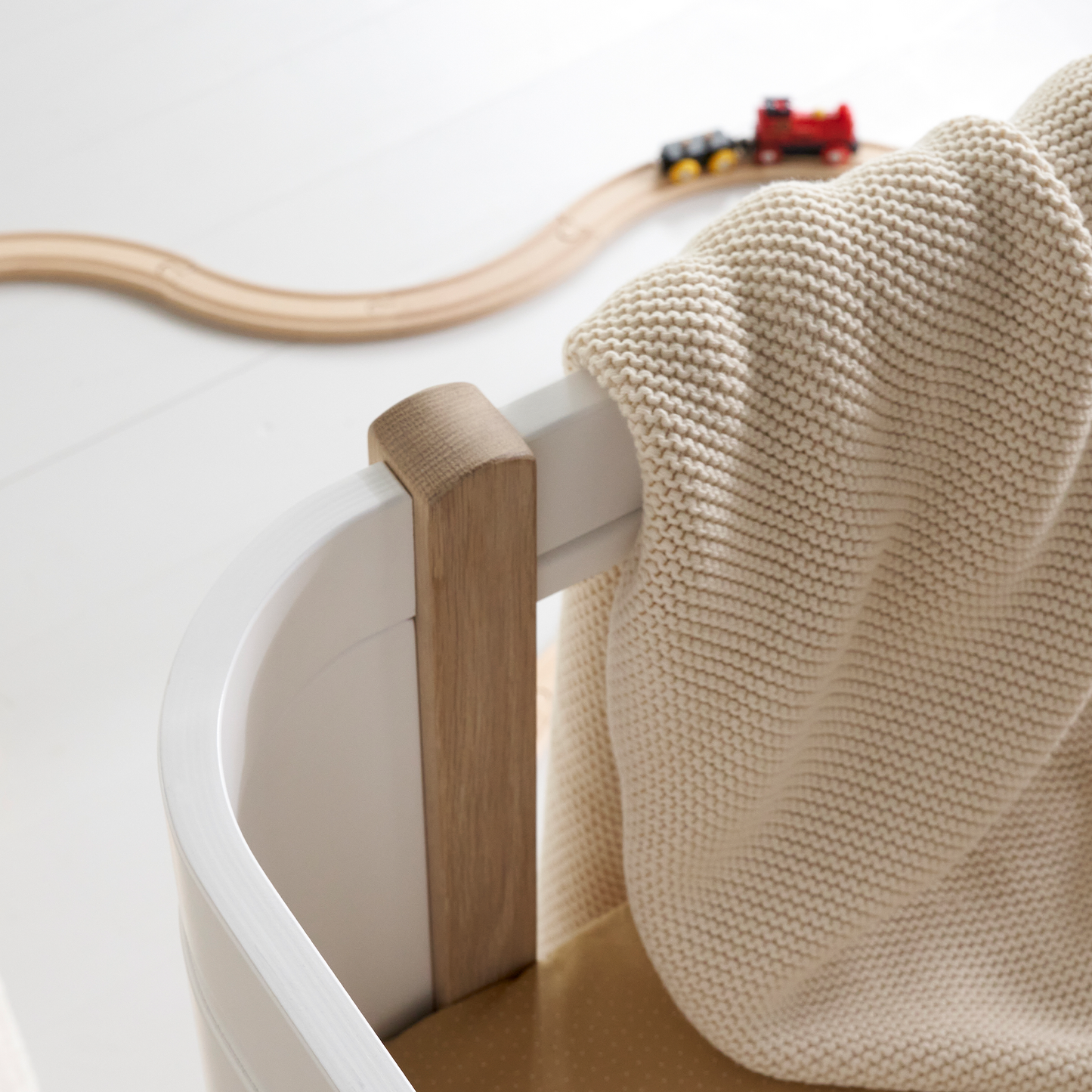 Children's toy train set on a white surface with a wooden toy track and a beige blanket.
