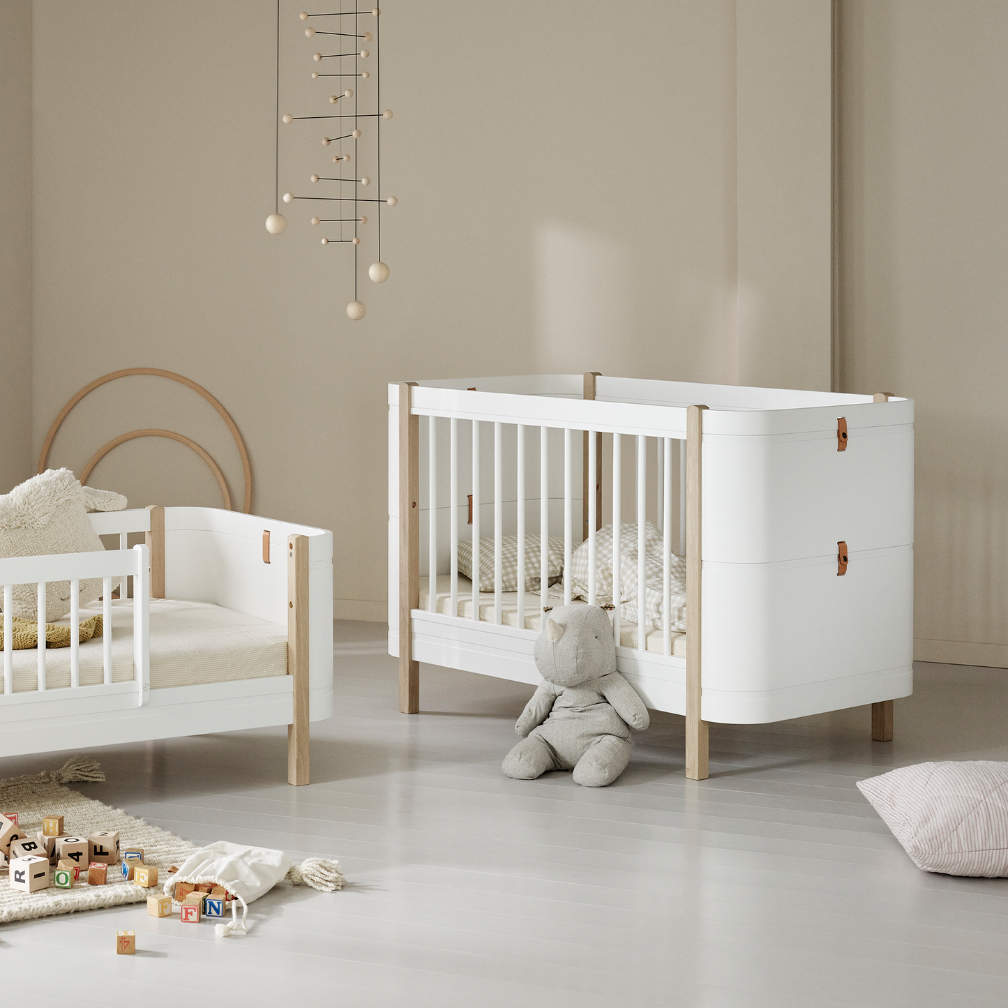 Nursery room with white crib and wooden bed frame on a light gray floor.