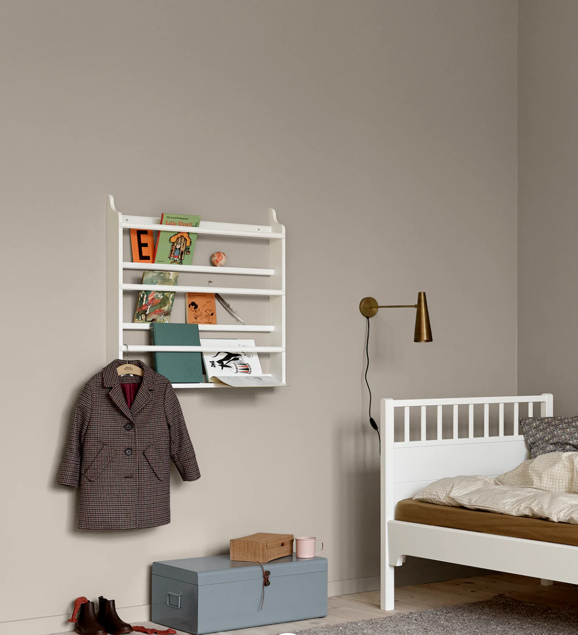 Children's room with a white bookshelf, coat, and bed against a beige wall.