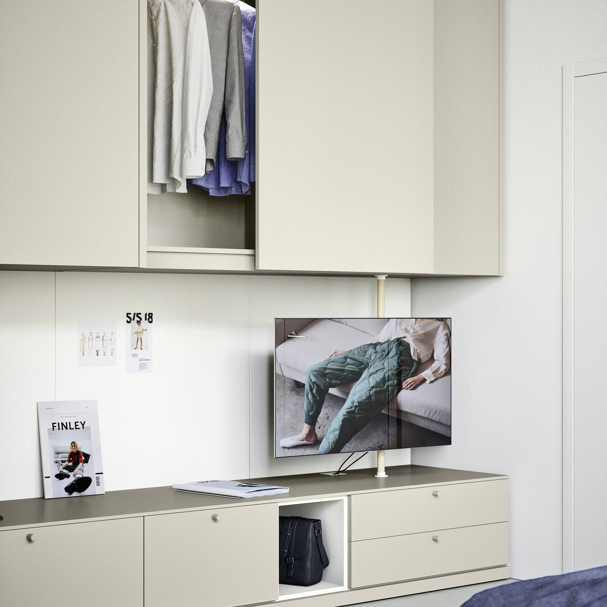 A modern beige wardrobe and storage cabinet system in a bedroom, with upper doors open to show hanging clothes and a lower cabinet holding a TV and accessories.