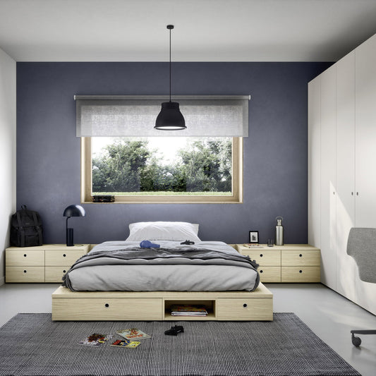A modern bedroom featuring a light wood platform bed with a gray and white bedding set, set against a dark slate blue-gray accent wall. The room includes a matching light wood nightstand, a large white wardrobe, a gray rug, and a black pendant light.