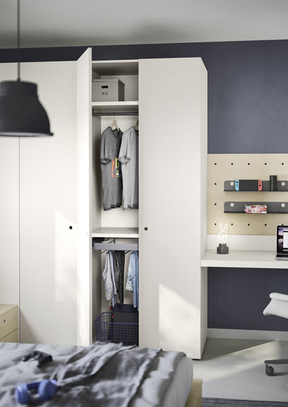 A Teen modern white wardrobe with one door open, showing hanging gray shirts and a storage box inside, set in a bedroom with a dark navy wall, desk, and pegboard.