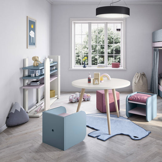 Children's room with a blue chair, pink ottoman, and round table near a window.