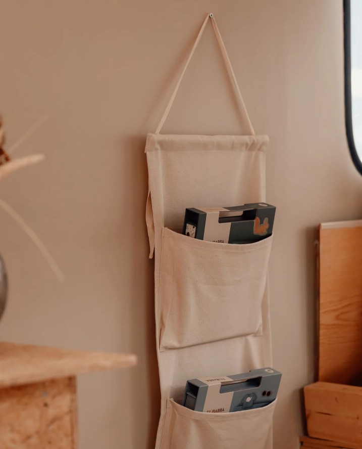 Beige wall-mounted storage bag with items inside hanging on a beige wall.