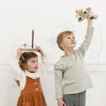Two children standing indoors, one holding a toy, against a white wall.