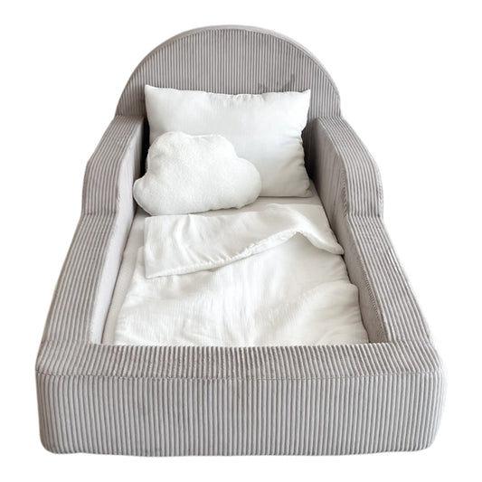 A small upholstered kidst bed with a gray corduroy-like striped fabric, shown empty with white bedding and two white pillows inside. 