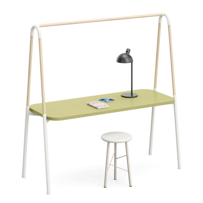 A minimalist desk with a light sage green top, white metal legs, and natural wood A-frame supports, accompanied by a white stool and a black desk lamp on a clean white background.
