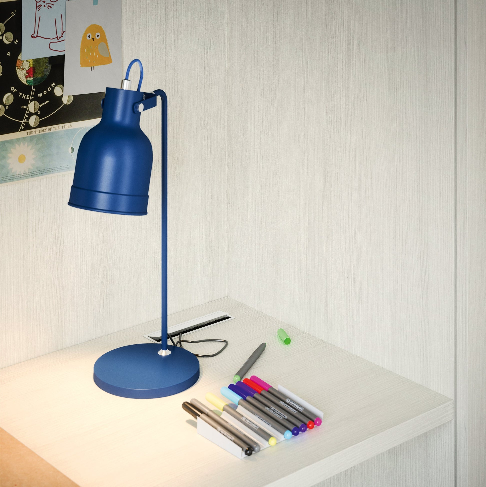 Close-up of Nidi Kids Space 12 desk with blue lamp, stationery and pale wood finish.