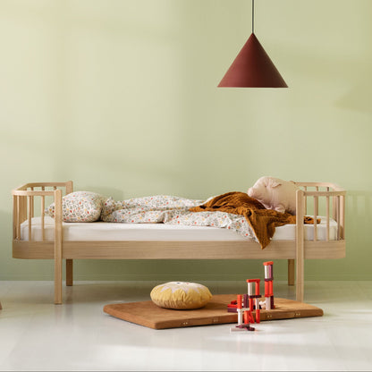A styled children's bedroom scene with a light wood single bed, pale green walls, a small white desk, and a hanging pendant lamp.