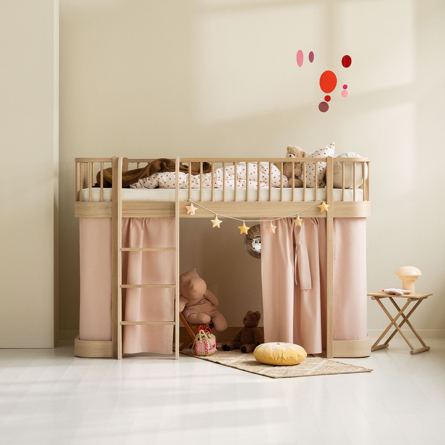 Children's room with a wooden loft bed, pink curtains, and toys on a light floor.