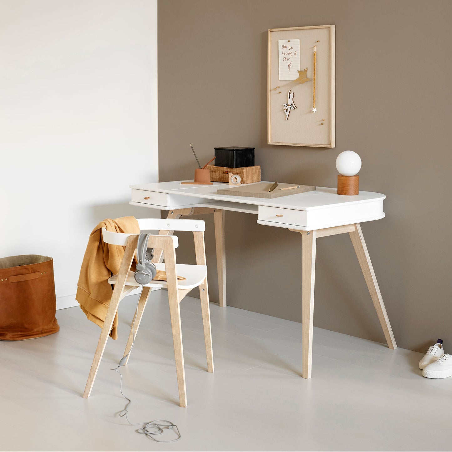 Minimalist home office with a white desk, wooden chair, and framed artwork on a gray wall.