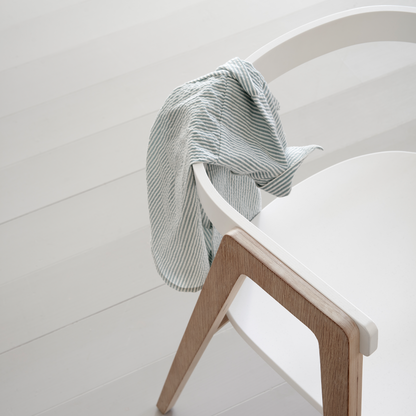 White chair with wooden legs draped with a striped towel on a light gray floor.