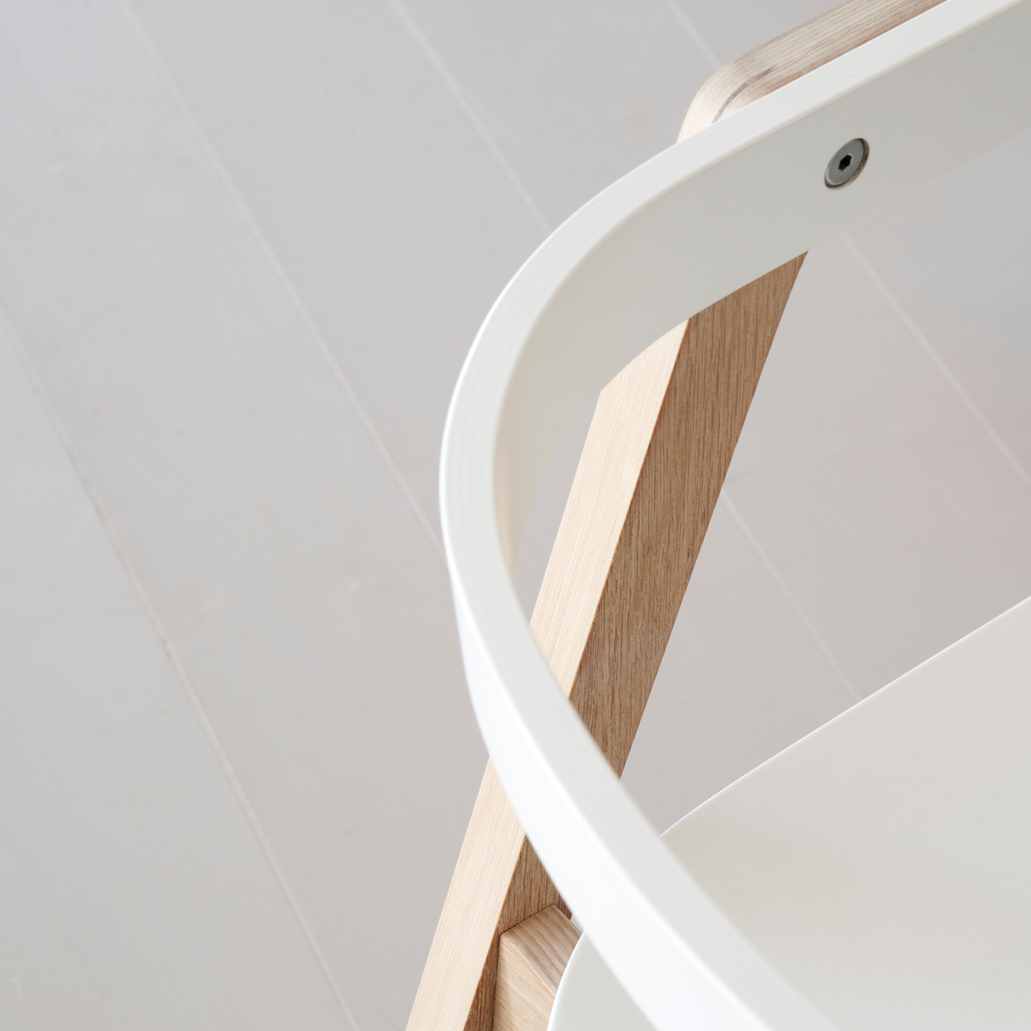 Close-up of a white spiral staircase with wooden balusters against a light gray wall.