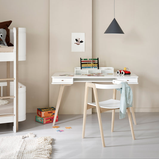 Children's room with a white desk, chair, and shelves against a beige wall.