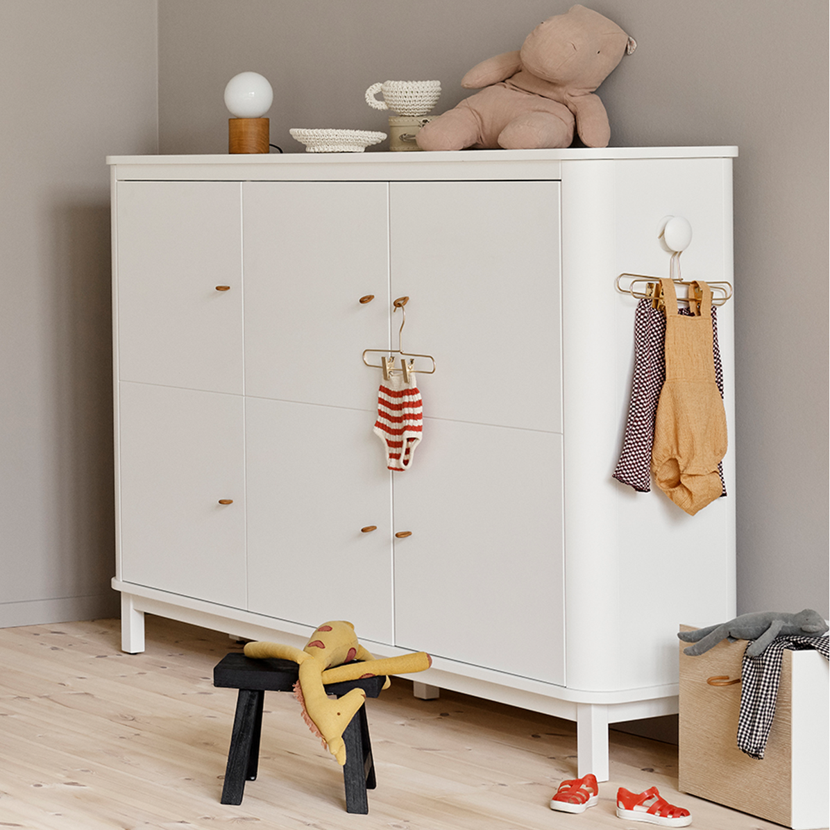 Nursery room with white dresser, crib, and toys on a light wooden floor.