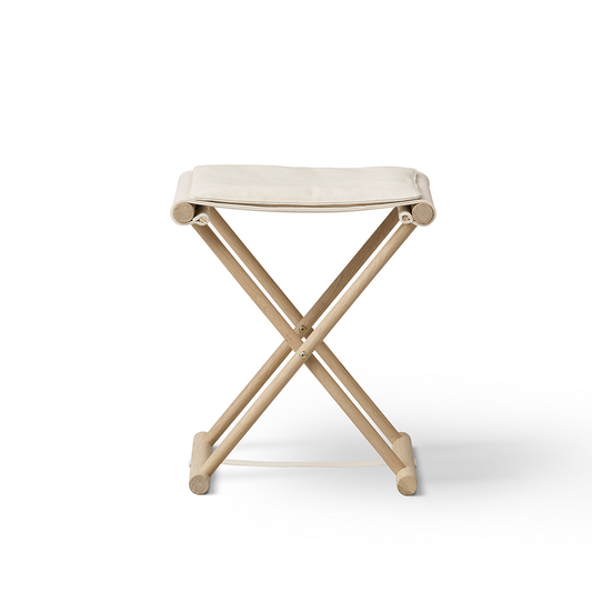 A compact folding stool with a light beige fabric seat and a natural wood X-frame base, shown on a clean white background.