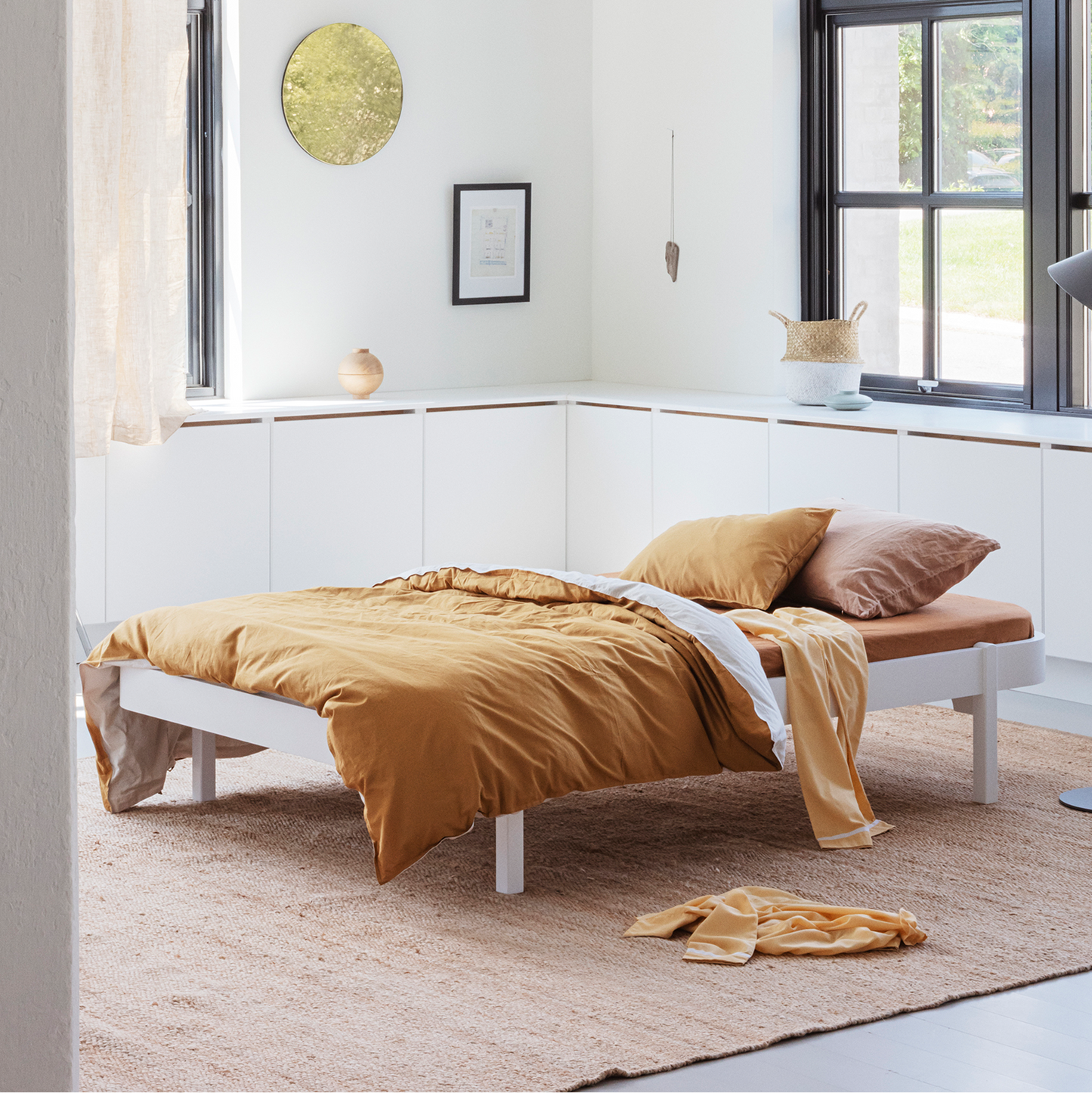 Modern bedroom with a bed covered in yellow bedding, white walls, and large windows.