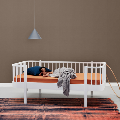White junior daybed with wooden mattress against a brown wall with a pendant light.