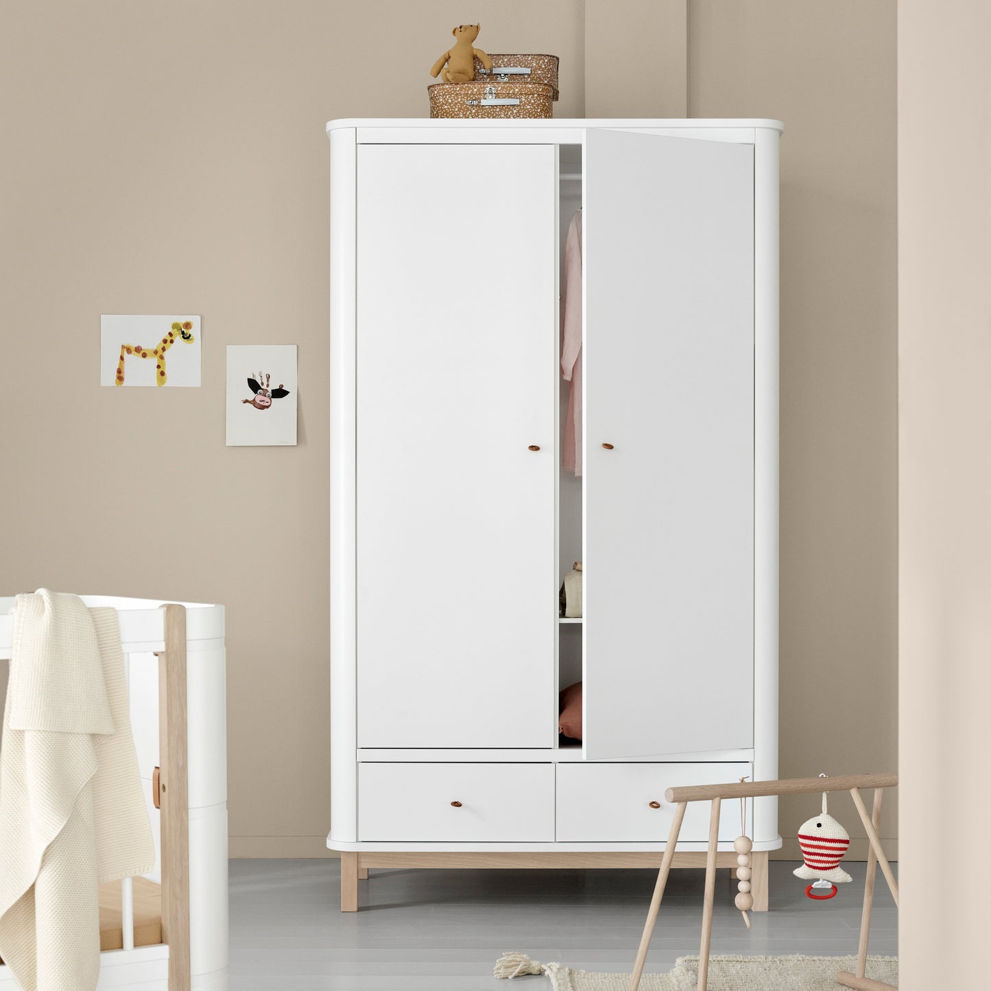 White wardrobe in a room with a crib and toys on a light gray floor.