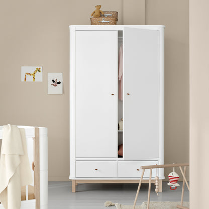 White wardrobe in a room with a crib and toys on a light gray floor.