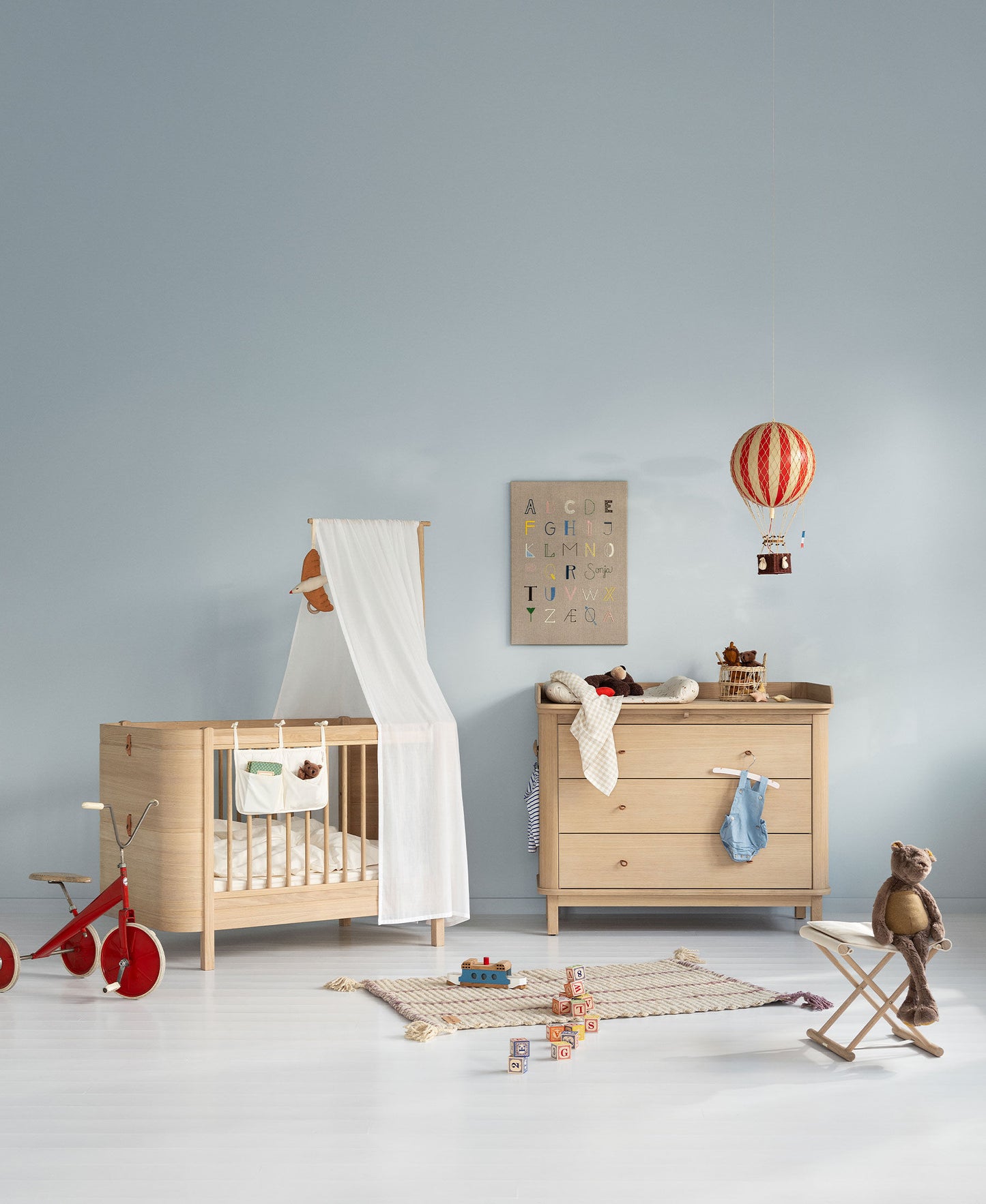 Nursery room with wooden crib, dresser, and toys against a light blue wall.
