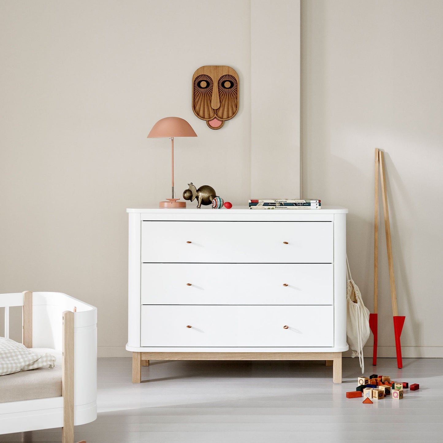 White dresser with wooden accents in a minimalistic room with toys and a lamp.