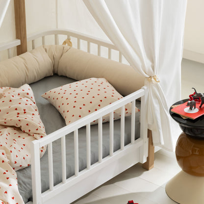 Children's bed with white canopy, gray mattress, and red heart-patterned pillows in a room with toys on the floor.