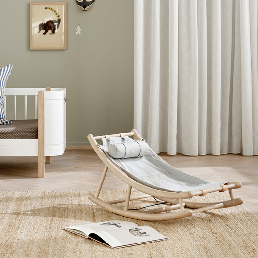 Nursery room with a rocking chair, crib, and framed pictures on a light green wall.