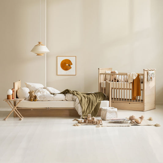 Nursery room with wooden crib and bed, neutral decor, and soft lighting.