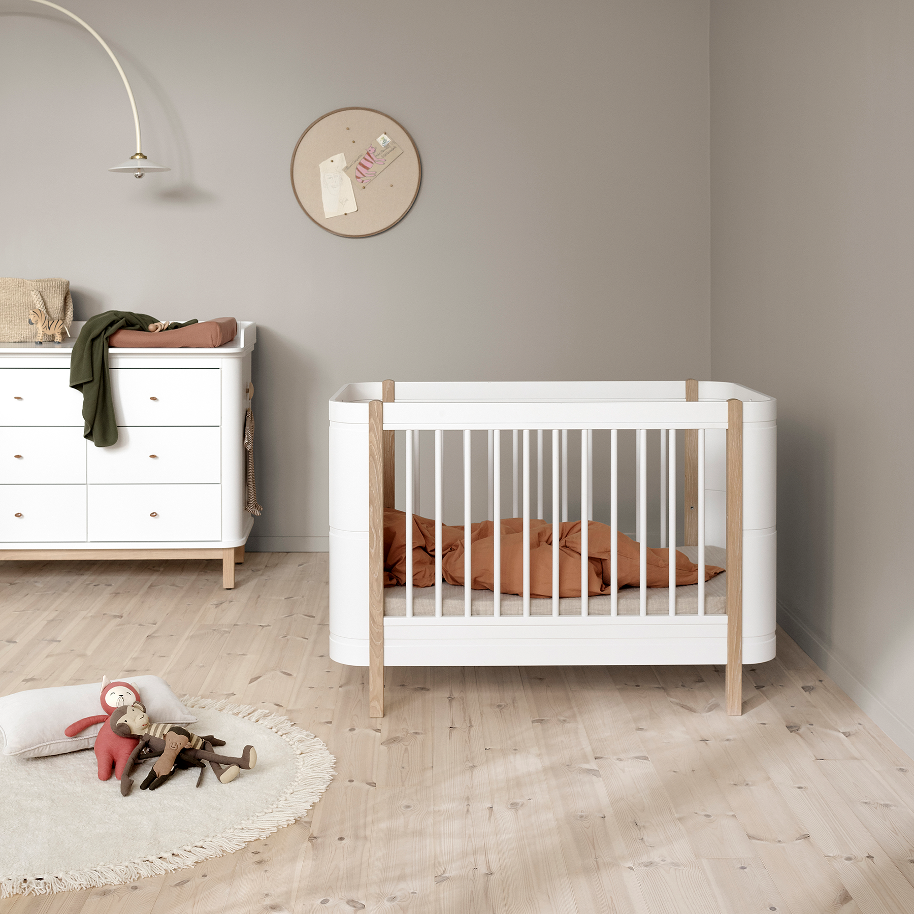 Nursery room with a white crib and dresser against a gray wall.