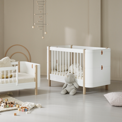Nursery room with white crib and wooden bed frame on a light gray floor.