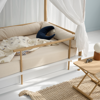Children's bed with wooden frame and white canopy in a bright room.