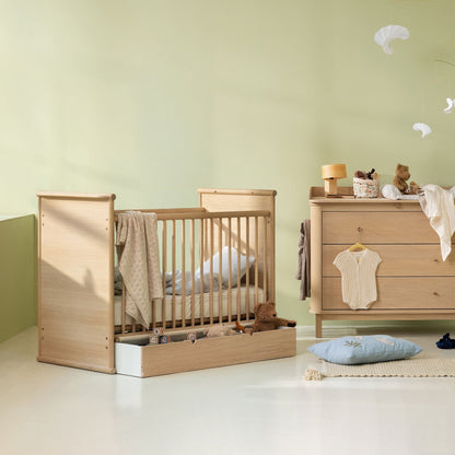 Nursery room with wooden crib and dresser against a light green wall.