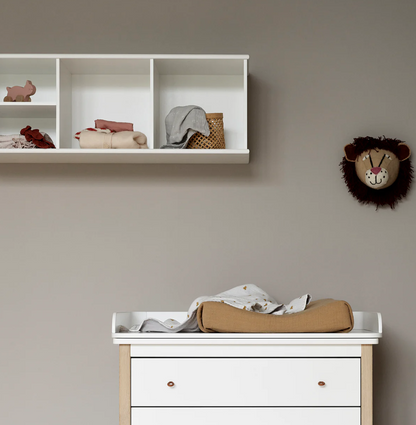 Nursery with a changing table, shelves, and decorative items on a beige wall.