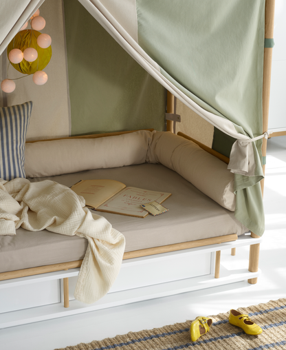 Children's reading nook with a cushioned bench, books, and a blanket inside a green and beige tent-like structure.