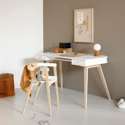 White desk with wooden chair against a wall with a framed picture