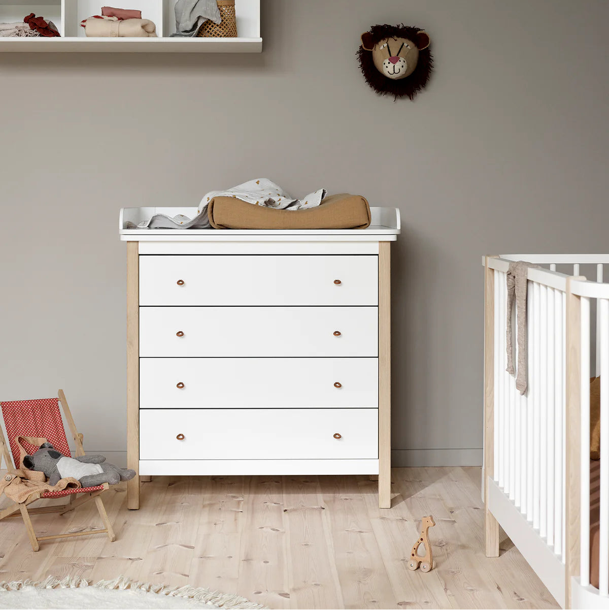 Nursery with white dresser, crib, and decorative items on a gray wall.