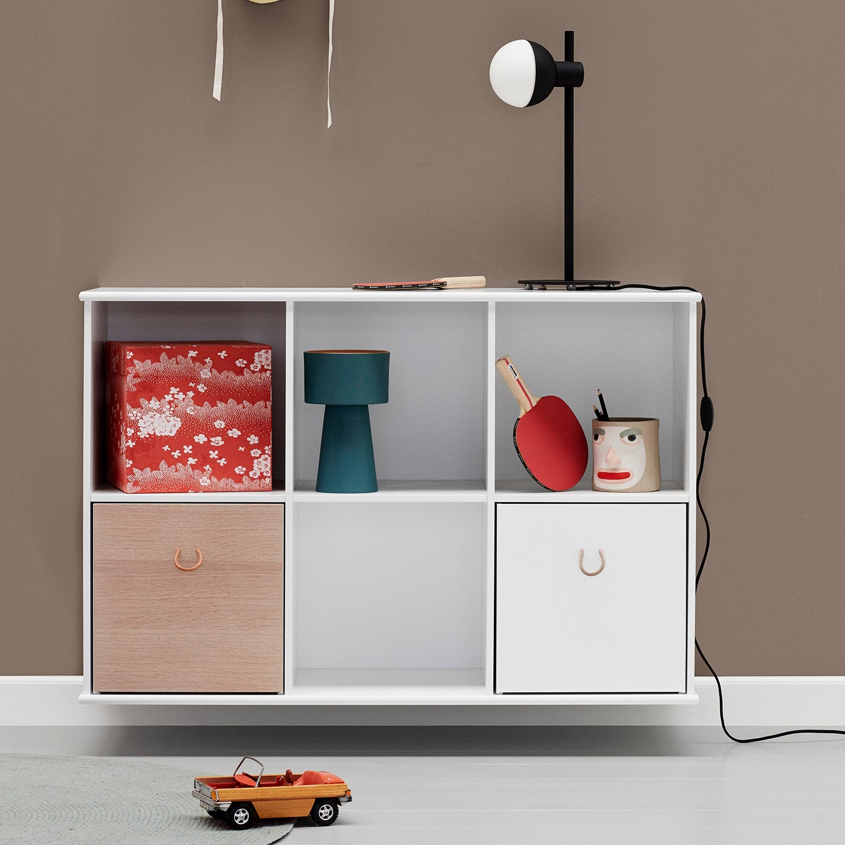White storage unit with wooden drawer against a brown wall, featuring toys and decorative items.