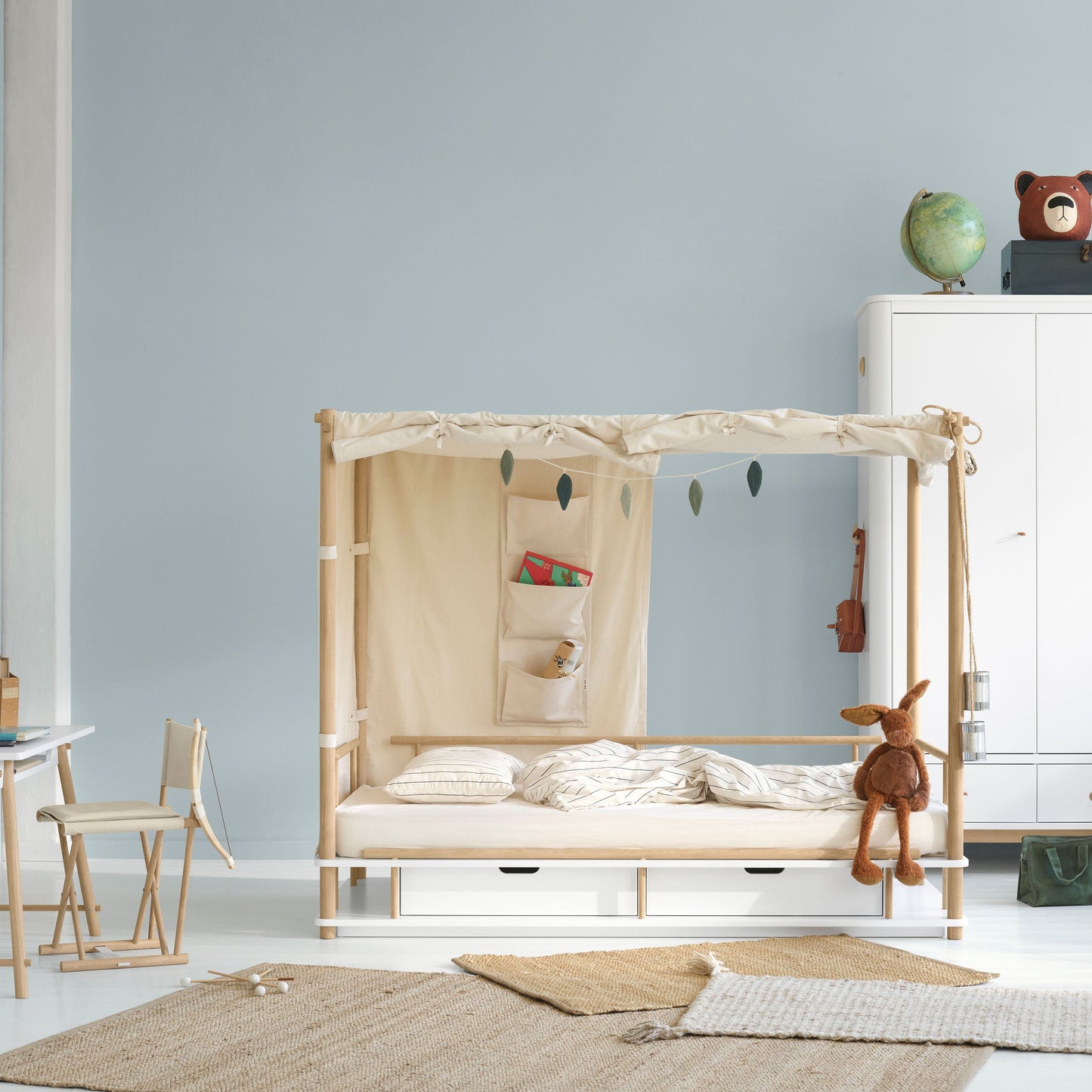 Children's room with a wooden crib, toys, and furniture against a light blue wall.