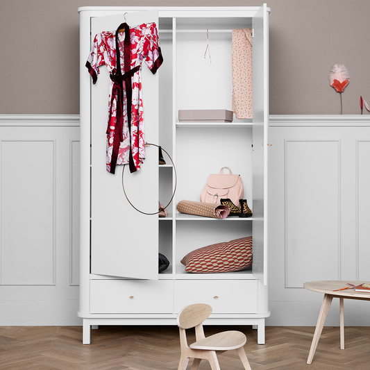 White wardrobe with clothes and bags in a room with a wooden floor and white walls.