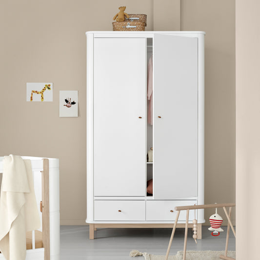 White wardrobe in a room with a crib and toys on a light gray floor.