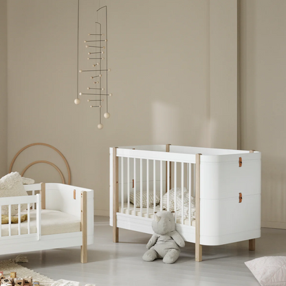 Children's room with white crib and wooden bed, beige walls, and toys on a light gray floor.