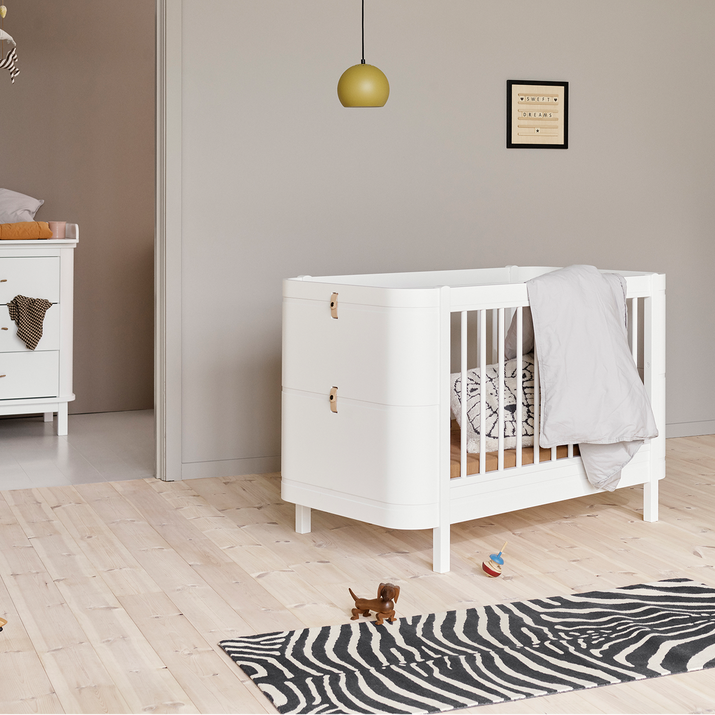 Nursery room with a white crib, dresser, and zebra print rug.