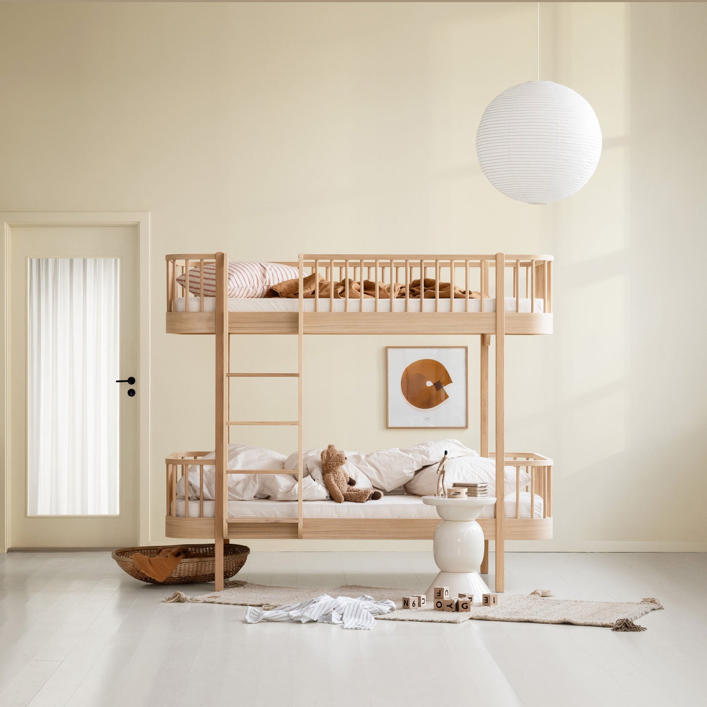 A light natural wood bunk bed with safety rails and a ladder, styled with neutral bedding and plush toys in a minimalist, warm-toned child's bedroom.