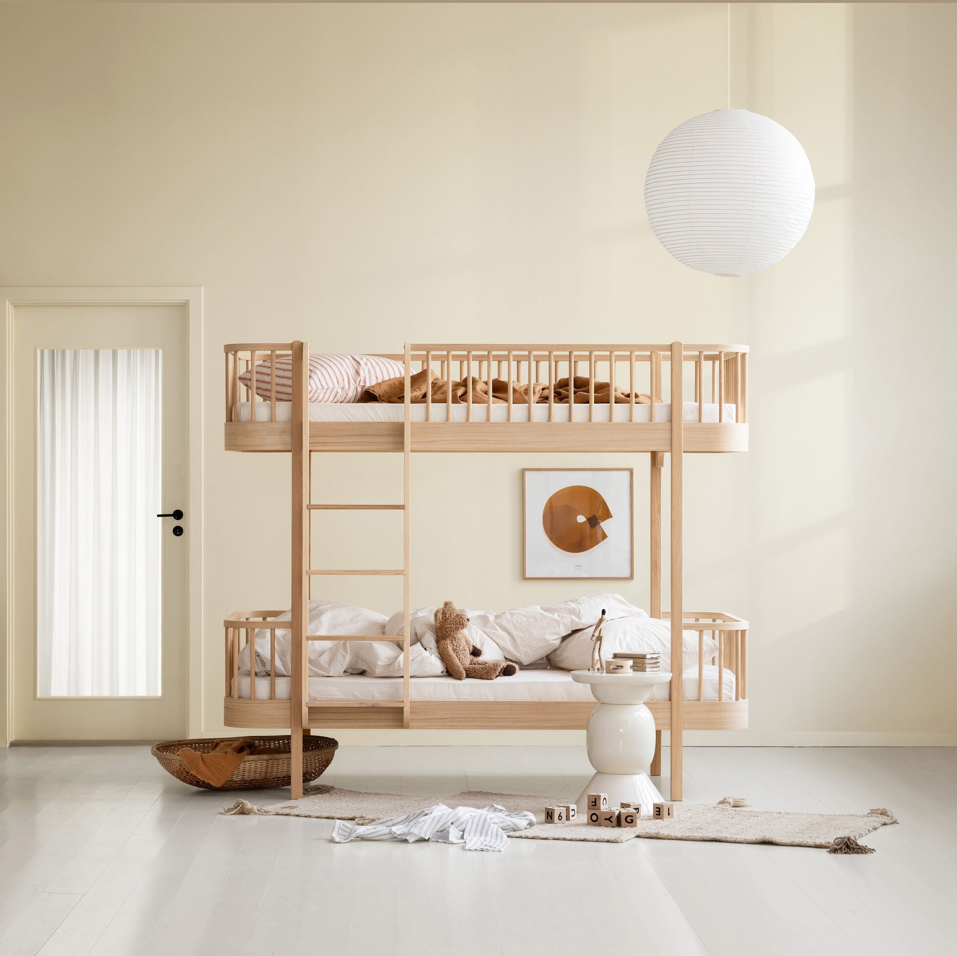 A light natural wood bunk bed with safety rails and a ladder, styled with neutral bedding and plush toys in a minimalist, warm-toned child's bedroom.