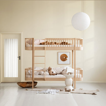 A light natural wood bunk bed with safety rails and a ladder, styled with neutral bedding and plush toys in a minimalist, warm-toned child's bedroom.